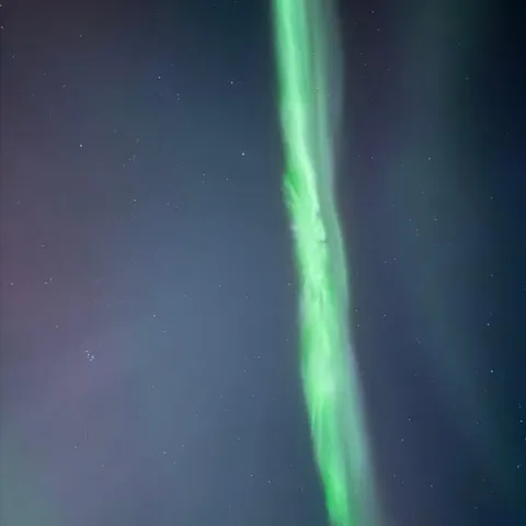 A bright green aurora column overhead