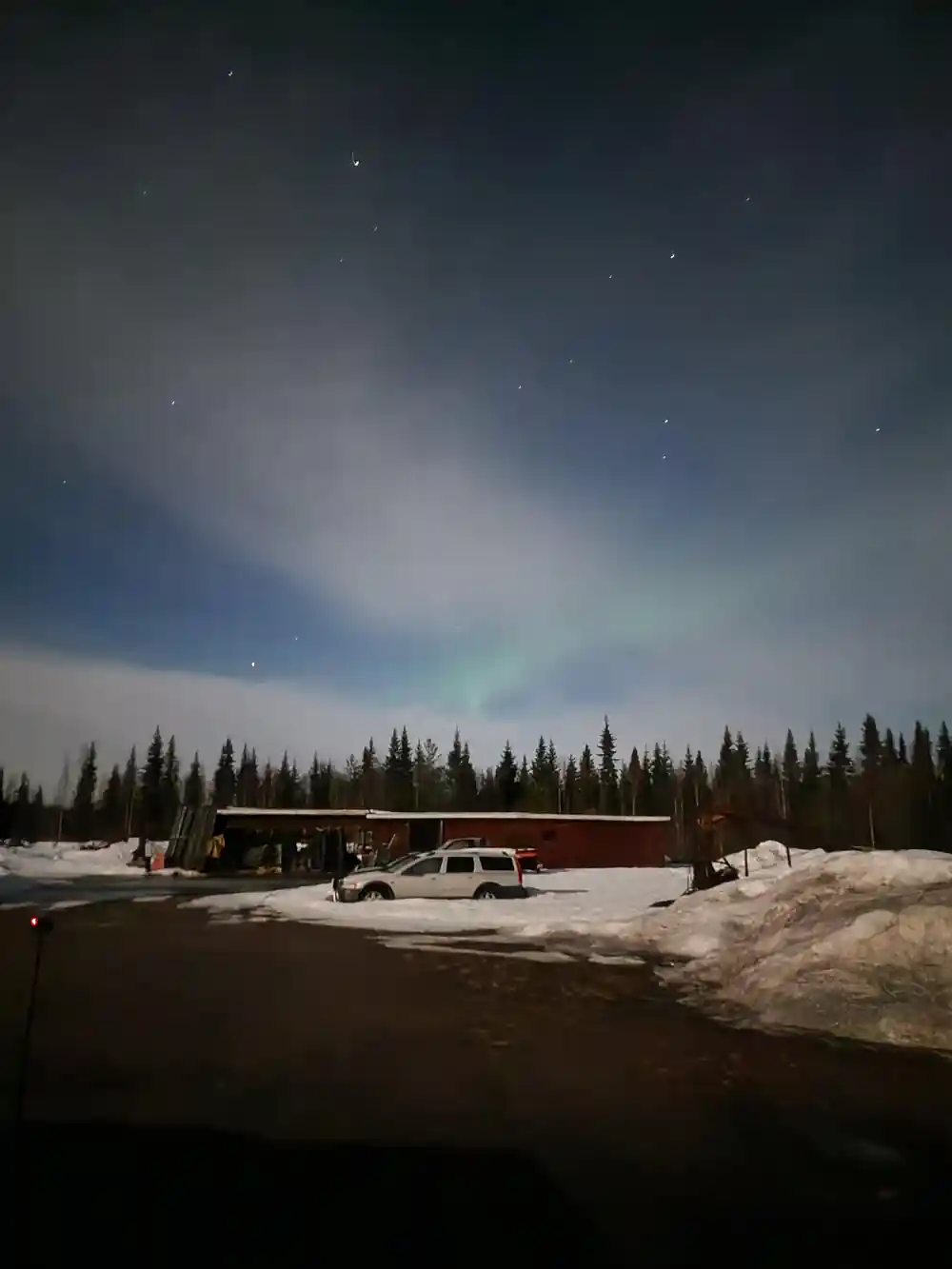 Aurora borealis over snowy landscape with buildings and vehicles