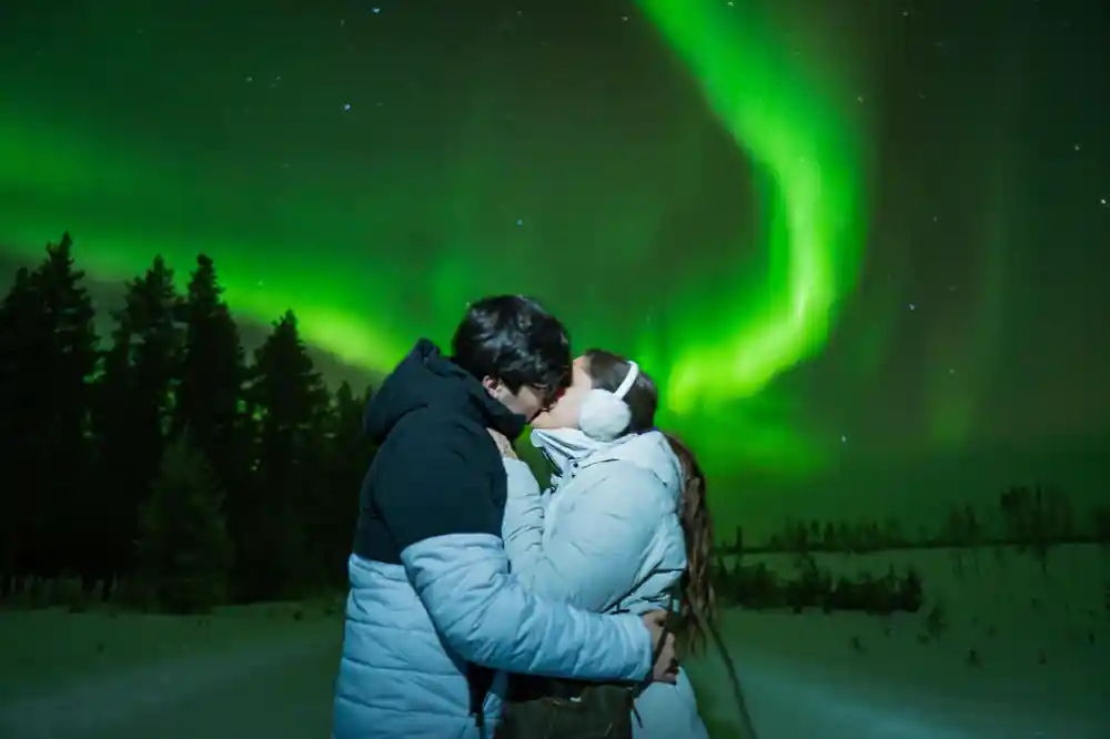 Couple kissing under curved green aurora display