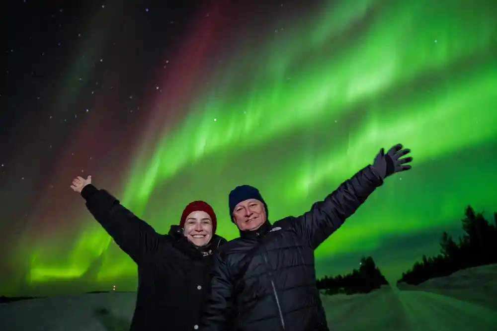 Couple with raised arms under green aurora borealis