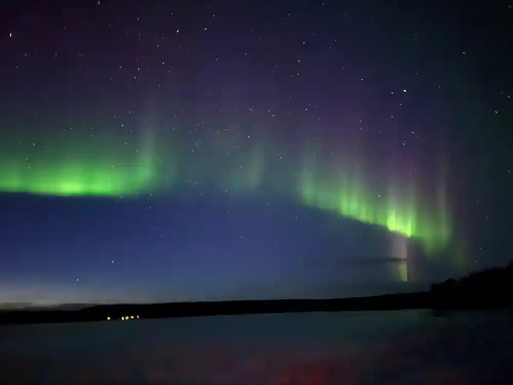 Green aurora borealis reflected in still water with forest