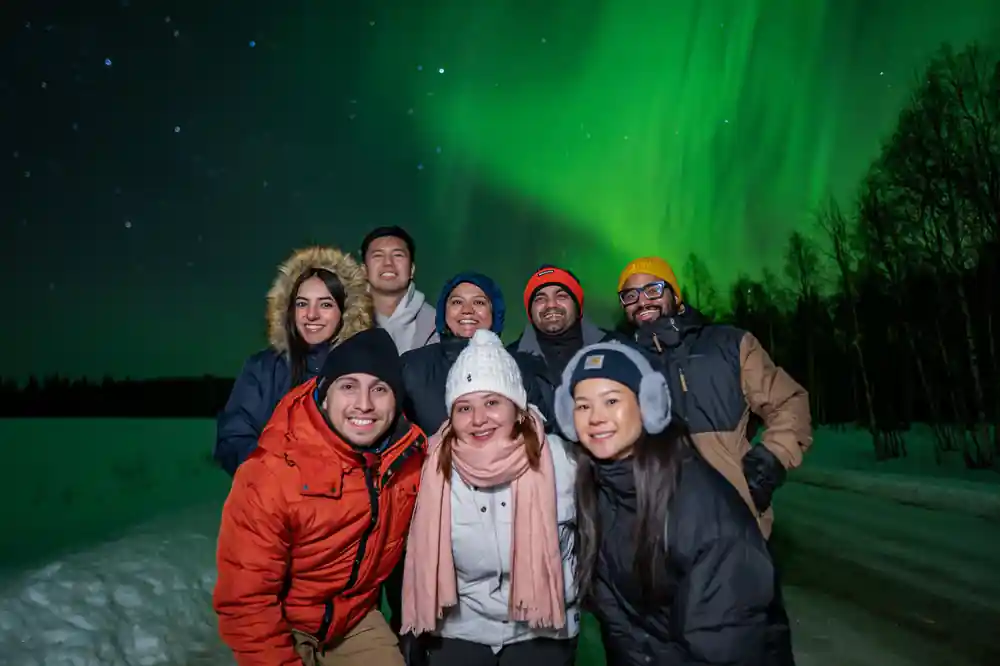 Group of people posing with green northern lights display