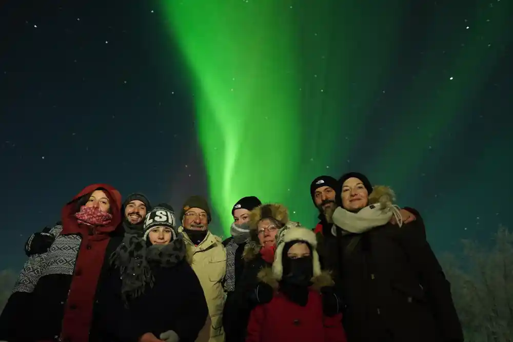 Group of people standing beneath green northern lights