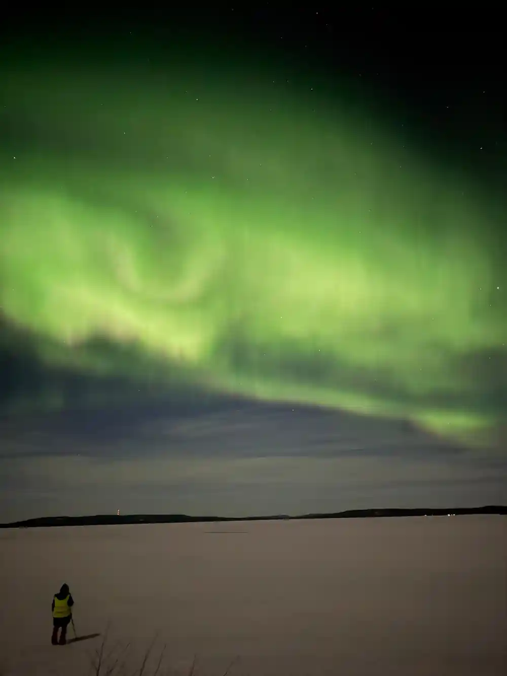Person in yellow jacket viewing aurora over frozen lake