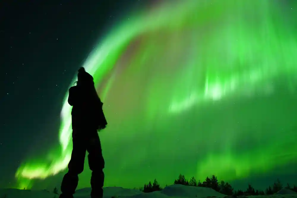 Silhouetted figure standing under swirling green aurora