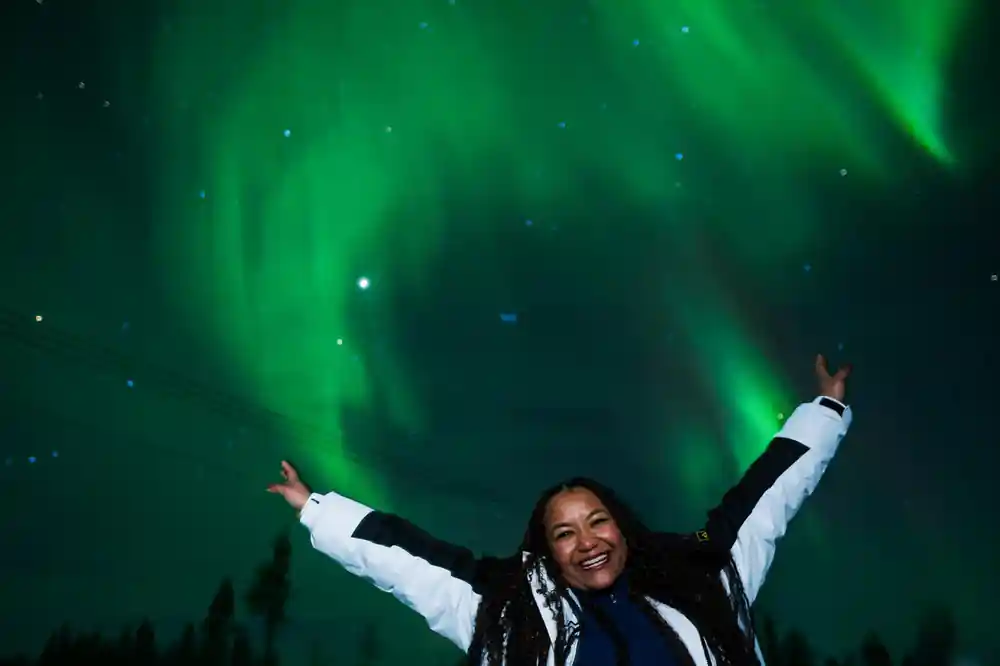 Single person with arms raised under bright green aurora