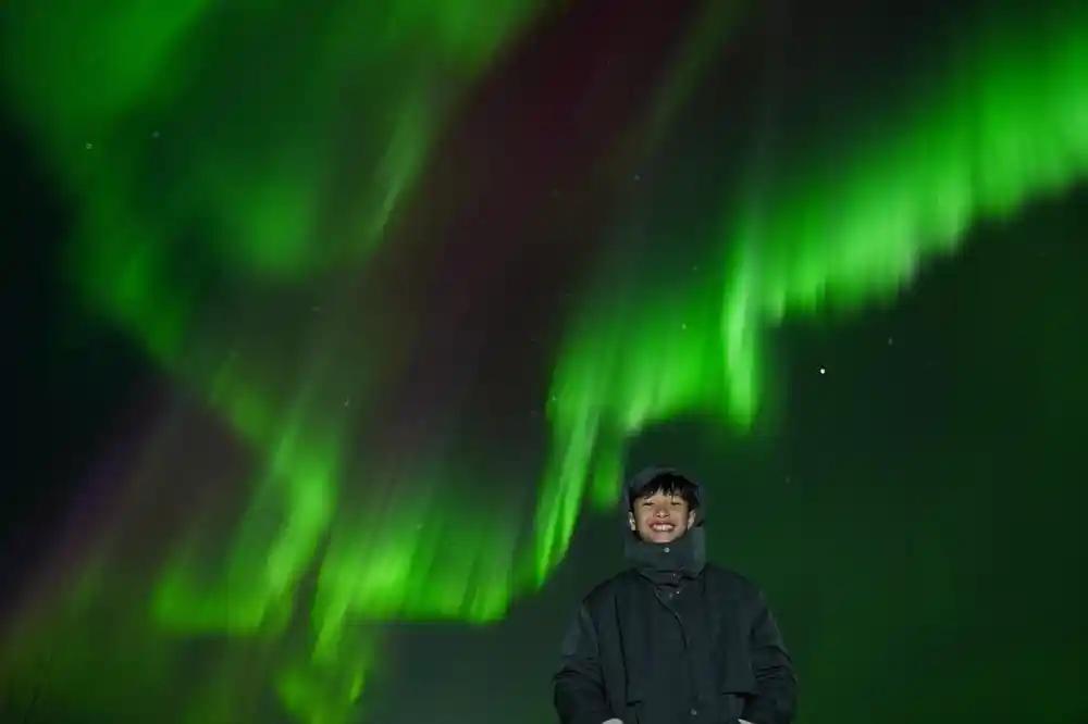 Single person standing beneath intense green northern lights