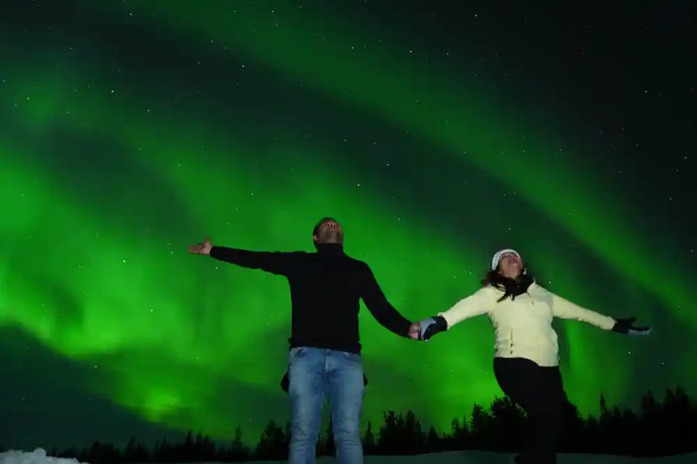 Two people holding hands under green aurora display