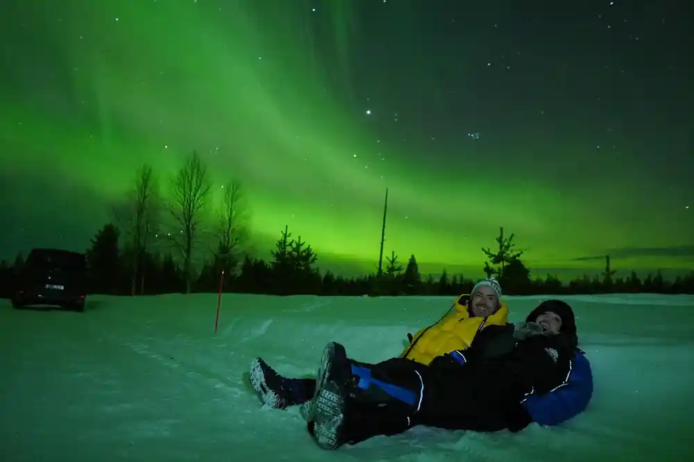 Two people lying on frozen lake beneath aurora