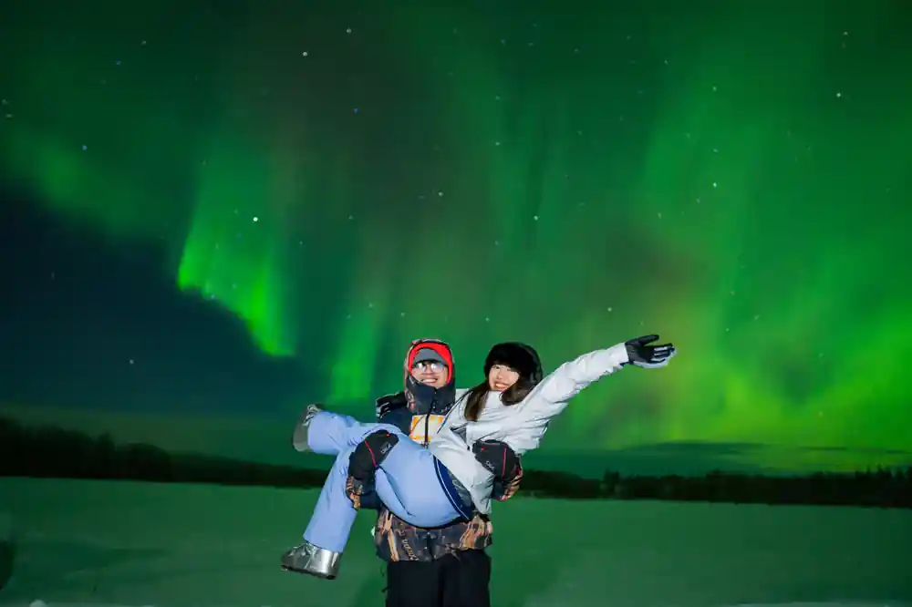 Two people playfully posing under green aurora display