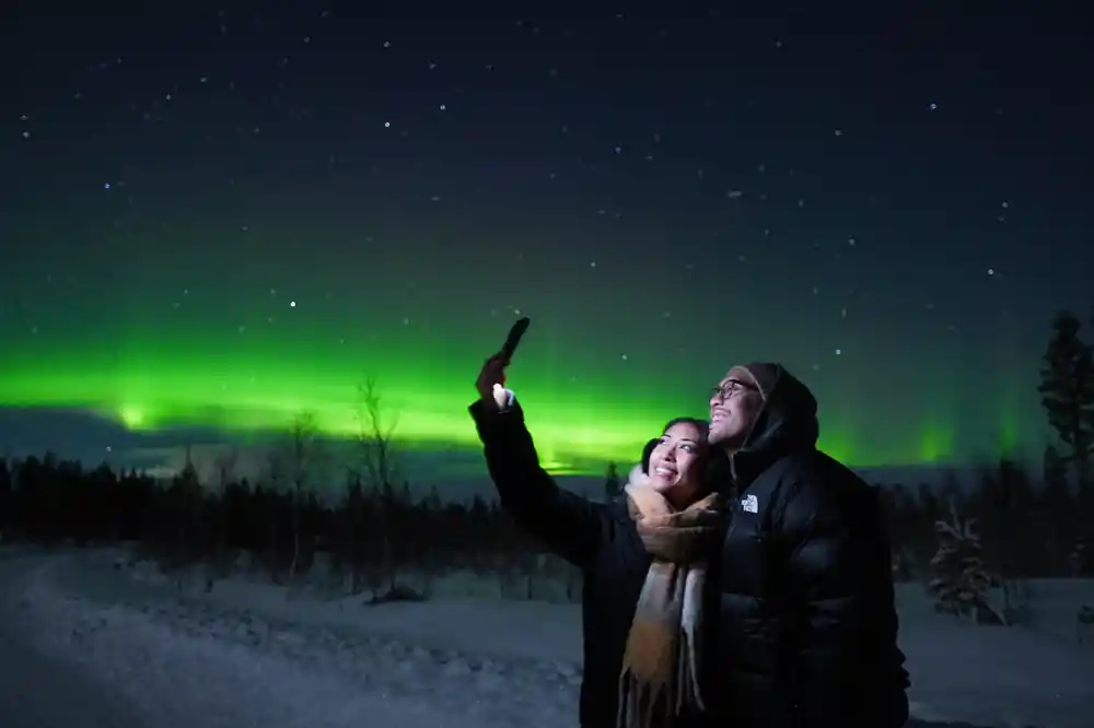 Two people pointing at aurora in snowy landscape
