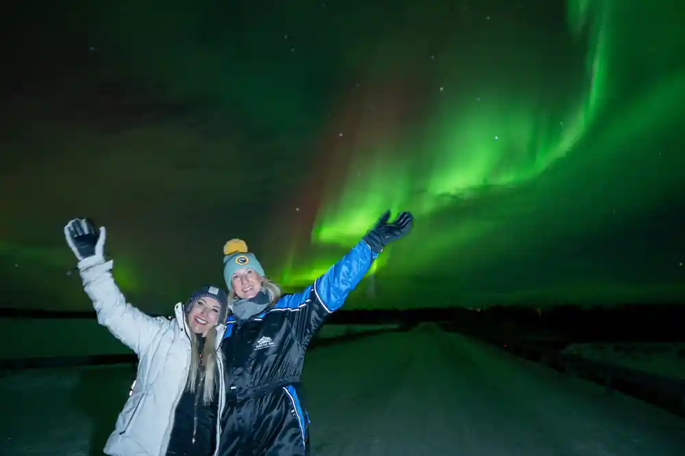Two people with raised arms under green northern lights