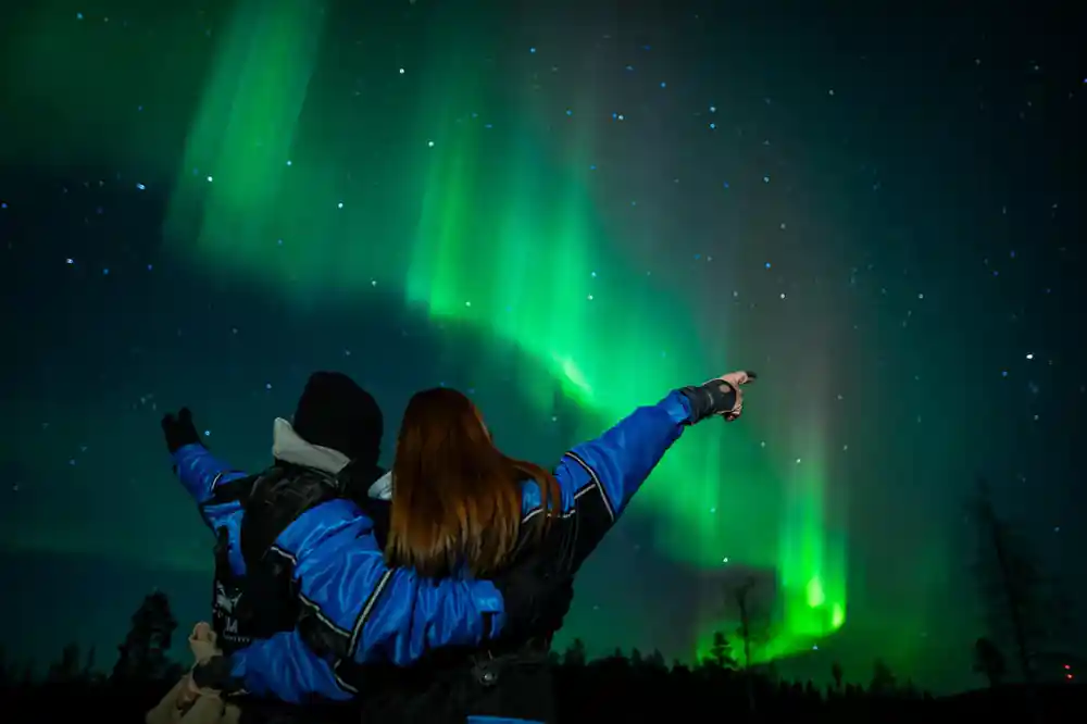 Woman pointing at bright green aurora in night sky